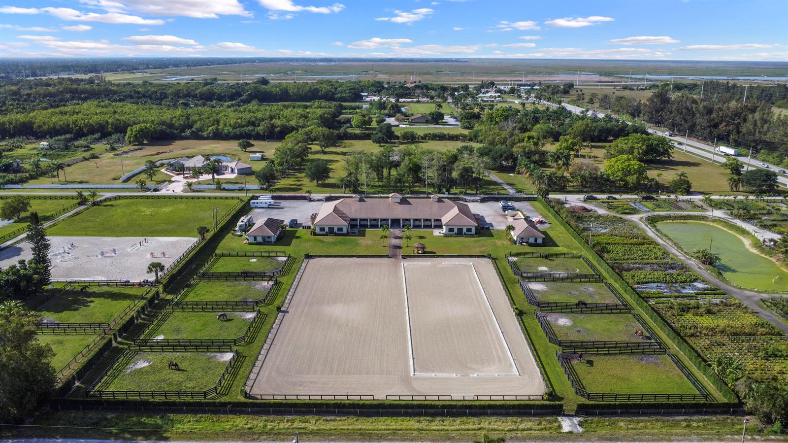 An aerial view of an equestrian property featuring a large stable, paddocks, and riding arenas — 16575 Van Gogh Road, Wellington FL 33414, WELLINGTON, FL