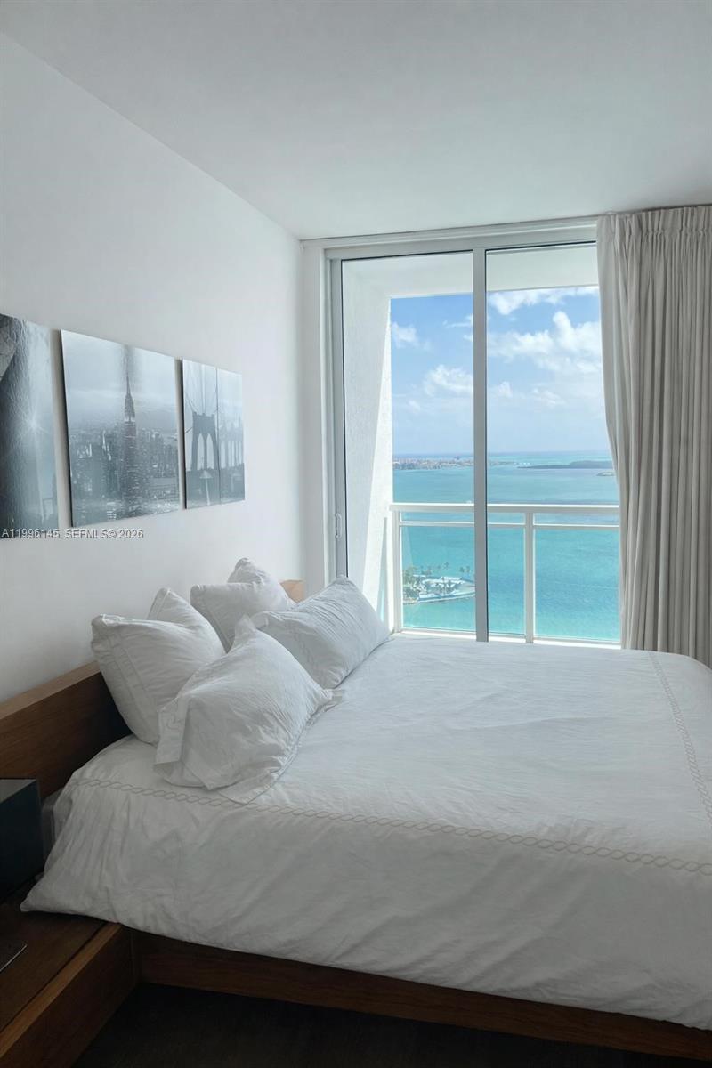A bedroom features a bed with white linens, wall art, and a balcony overlooking the ocean — 951 Brickell Ave # 3506, Miami FL 33131, MIAMI, FL