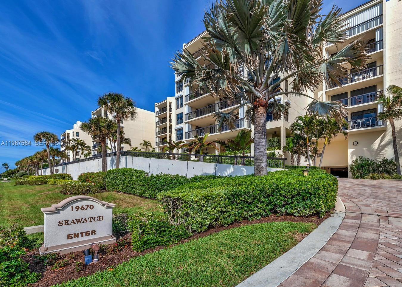 A multi-story residential building with balconies stands behind a landscaped lawn and entrance sign — 19670 Beach Rd # B323, Tequesta FL 33469, TEQUESTA, FL