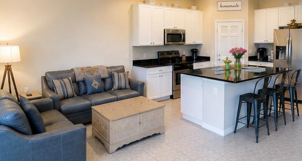 An open-concept kitchen with white cabinets and a black island overlooks a living room area — 7024 WOODCHASE GLEN DRIVE, RIVERVIEW, FL