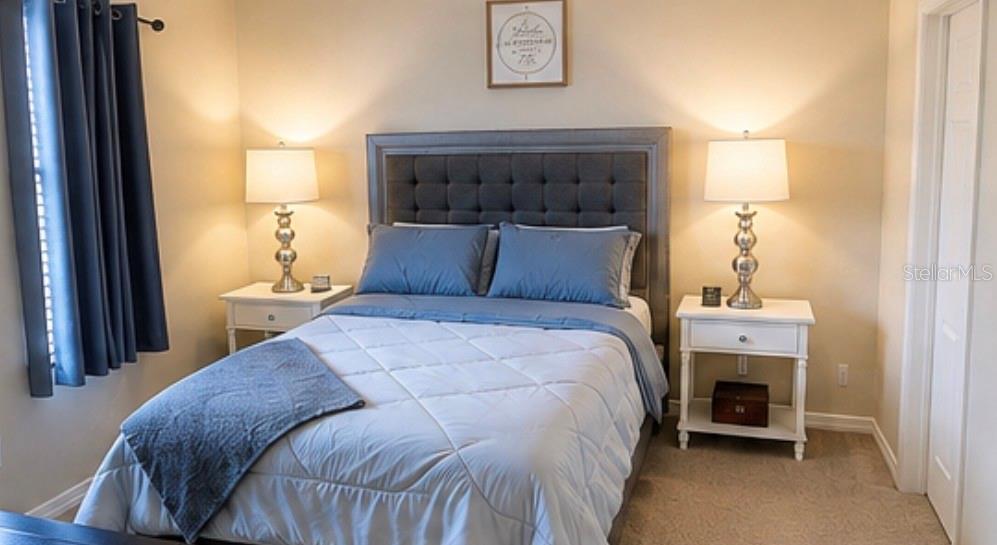 A bedroom features a tufted gray headboard, two white nightstands with lamps, and blue bedding — 7024 WOODCHASE GLEN DRIVE, RIVERVIEW, FL