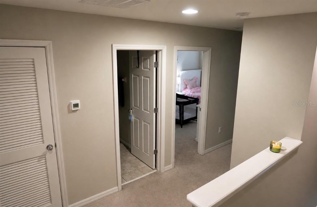 A hallway with beige walls, carpeted flooring, a louvered door, and two open doorways — 7024 WOODCHASE GLEN DRIVE, RIVERVIEW, FL