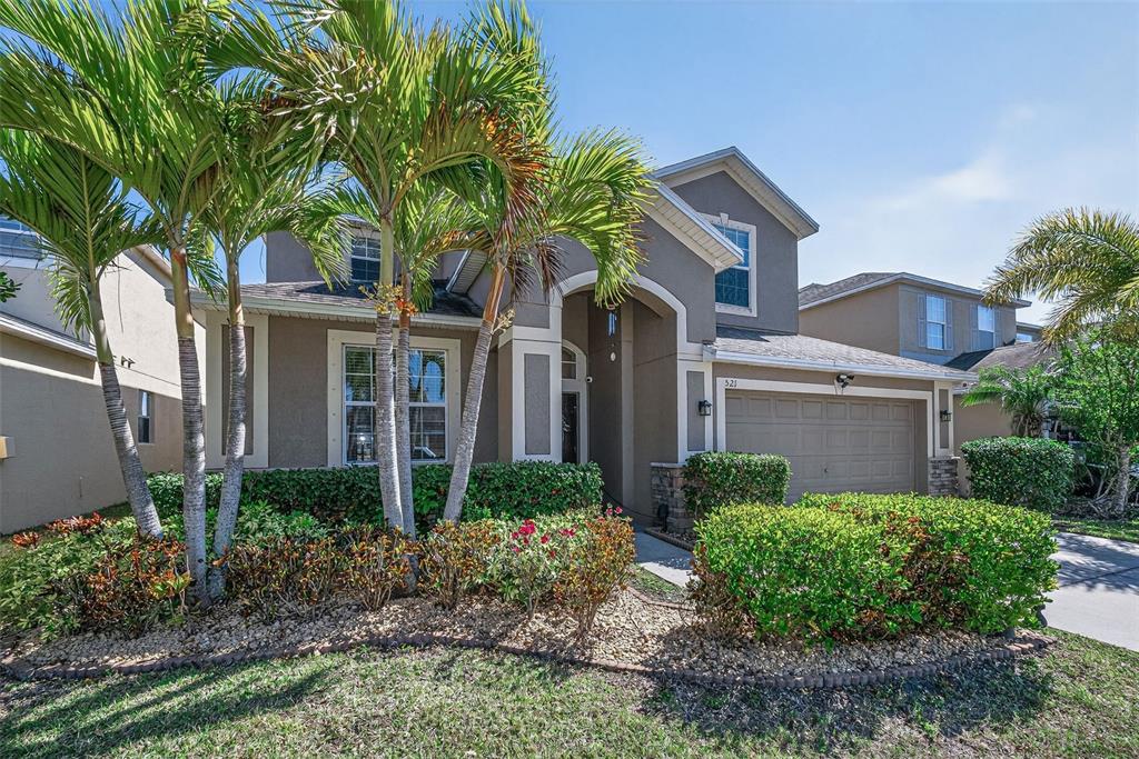 A two-story suburban house features a tan stucco exterior, a two-car garage, and palm trees — 521 VISTA RIDGE DRIVE, RUSKIN, FL
