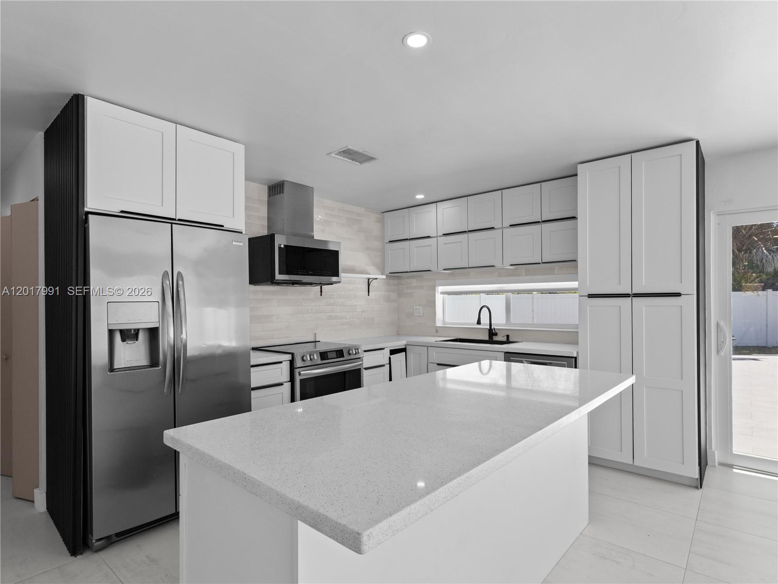 A modern kitchen features white cabinetry, stainless steel appliances, and a large quartz-topped island — 421 S 56th Ter, Hollywood FL 33023, HOLLYWOOD, FL
