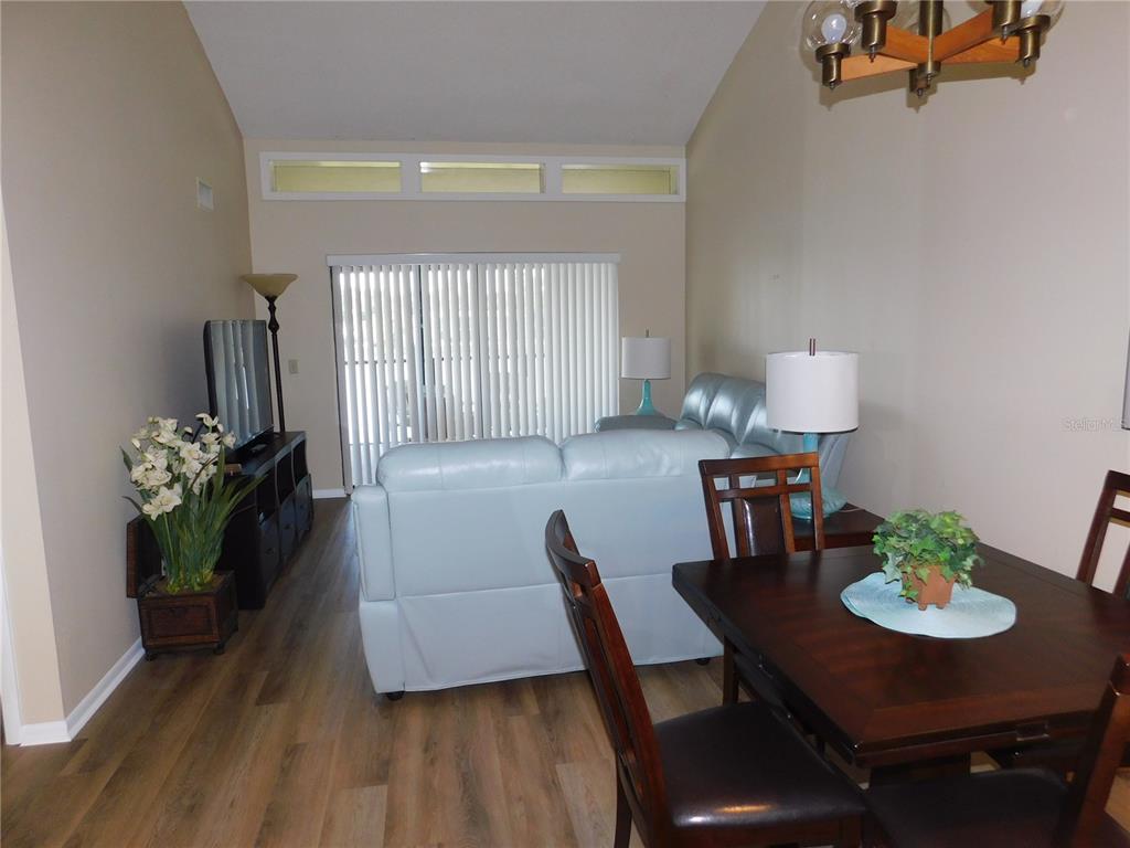 A living and dining area features wood-look flooring, vaulted ceilings, and a sliding glass door — 250 WOODLAKE WYNDE UNIT 250, OLDSMAR, FL