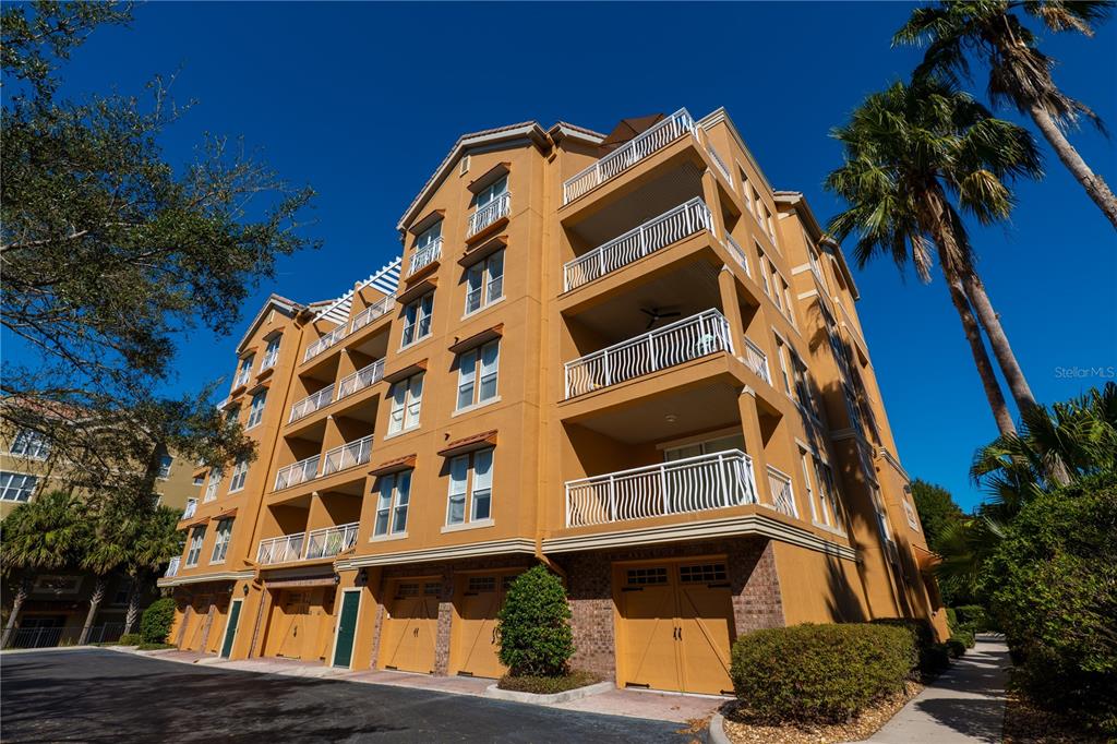A multi-story tan apartment building features private balconies and ground-level garage doors — 7500 TOSCANA BOULEVARD UNIT 341, ORLANDO, FL