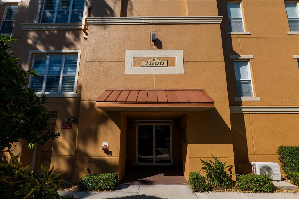 The exterior of a tan multi-story building features a central entrance under a metal awning — 7500 TOSCANA BOULEVARD UNIT 341, ORLANDO, FL