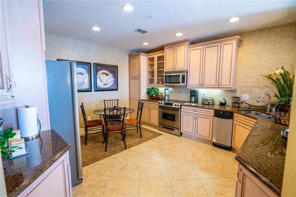 A kitchen features light-colored cabinets, granite countertops, stainless steel appliances, and a small dining area — 7500 TOSCANA BOULEVARD UNIT 341, ORLANDO, FL