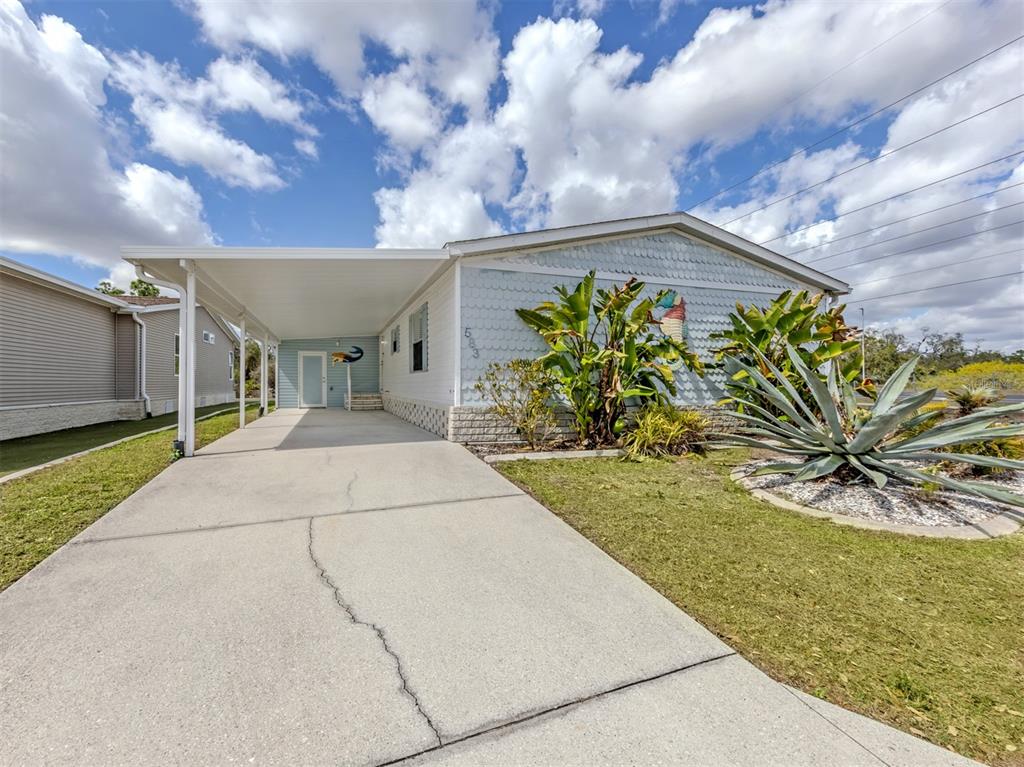 A single-story mobile home features a concrete driveway, a covered carport, and landscaped front yard — 583 PORTSIDE DRIVE, NORTH PORT, FL