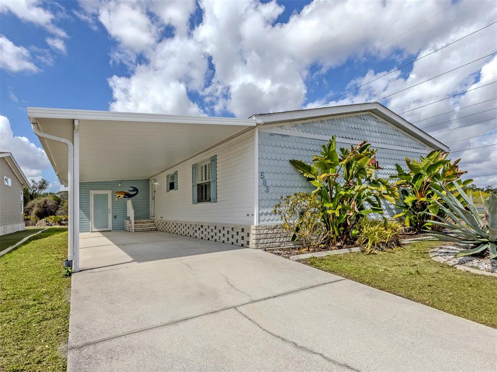 A single-story manufactured home features a concrete driveway, a carport, and light blue siding — 583 PORTSIDE DRIVE, NORTH PORT, FL