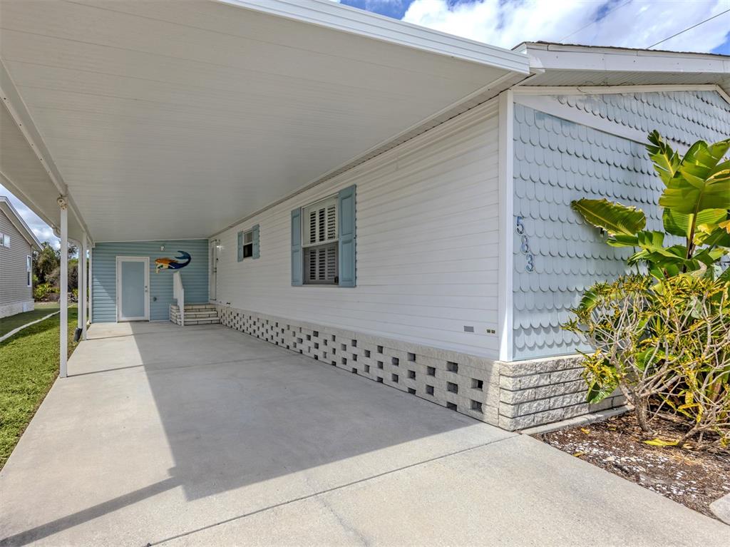 A white mobile home exterior features a concrete carport, blue shutters, and decorative scalloped siding — 583 PORTSIDE DRIVE, NORTH PORT, FL