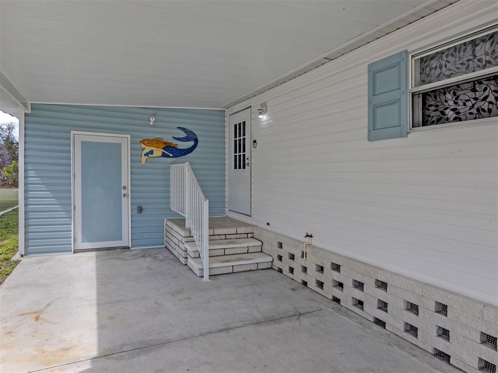 A concrete carport features a blue accent wall with a mermaid decoration and white siding — 583 PORTSIDE DRIVE, NORTH PORT, FL