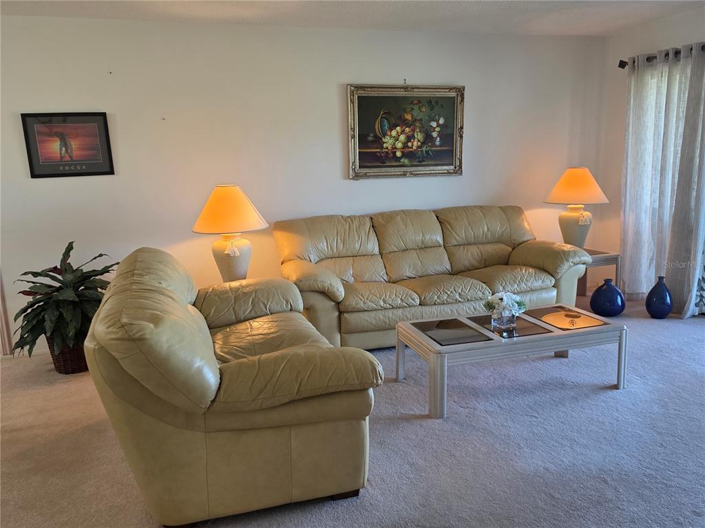 A living room features light-colored leather sofas, a coffee table, and two table lamps — 3500 EL CONQUISTADOR PARKWAY UNIT 260, BRADENTON, FL