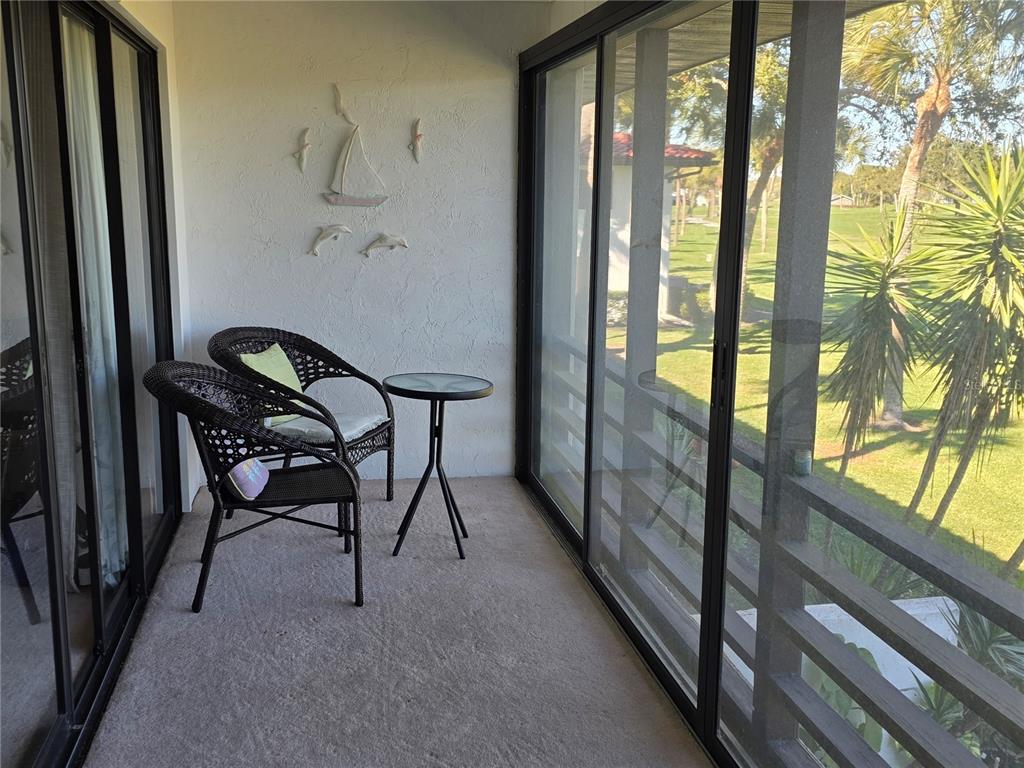 A screened-in balcony features two wicker chairs, a small table, and a view of greenery — 3500 EL CONQUISTADOR PARKWAY UNIT 260, BRADENTON, FL