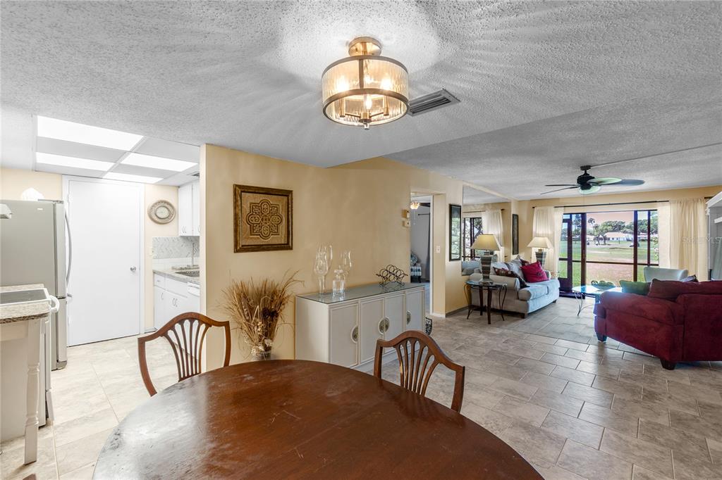 A dining area with a round wooden table opens into a living room with tile flooring — 4119 61ST AVENUE TERRACE W UNIT 102, BRADENTON, FL