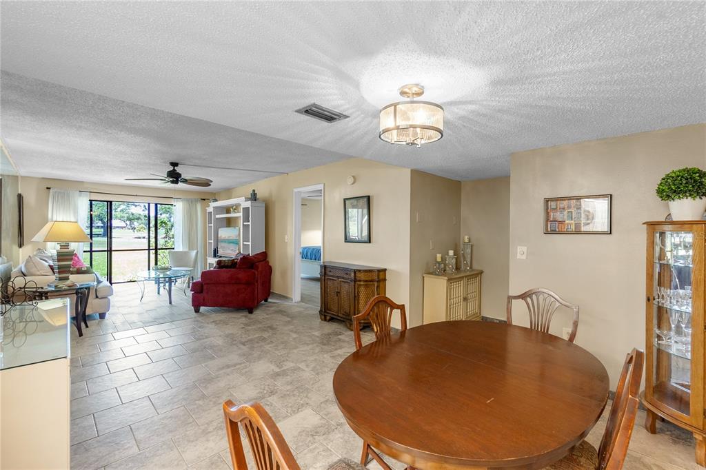 A dining area with a round wooden table opens into a living room with tile floors — 4119 61ST AVENUE TERRACE W UNIT 102, BRADENTON, FL