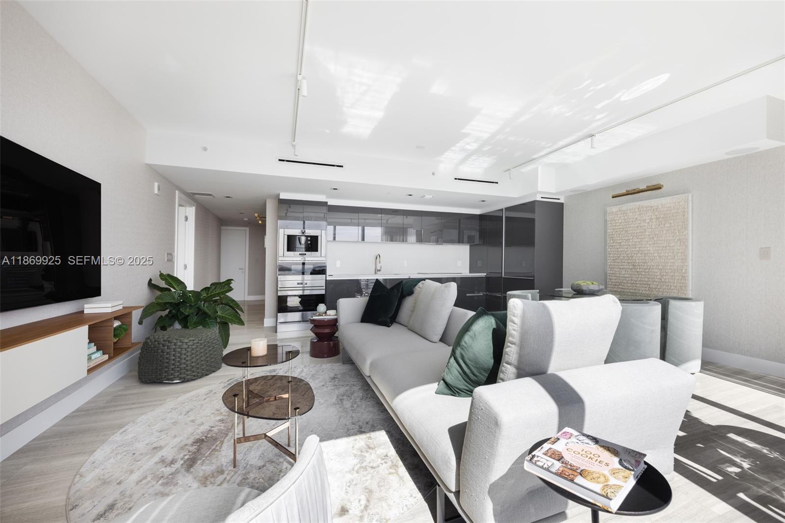 A modern open-concept living room features a grey sofa, kitchen cabinetry, and a television — 1451 Brickell Ave # 1901, Miami FL 33131, MIAMI, FL