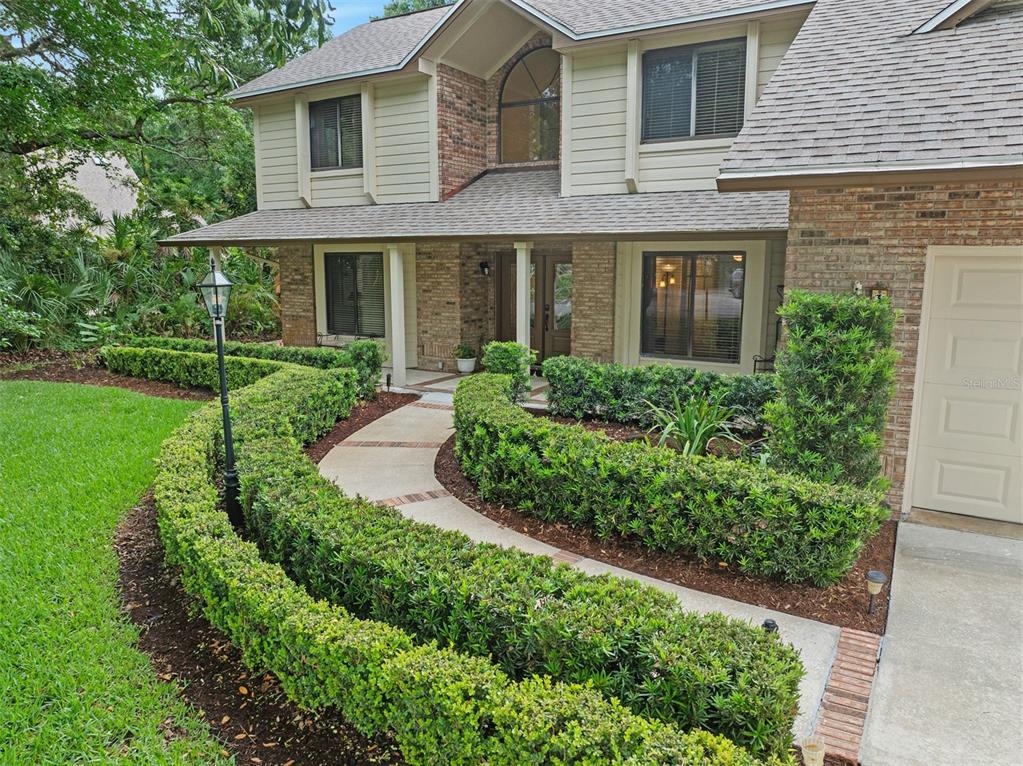 A two-story house with a brick and siding exterior features a curved hedge-lined walkway — 1 CROOKED BRIDGE WAY, ORMOND BEACH, FL