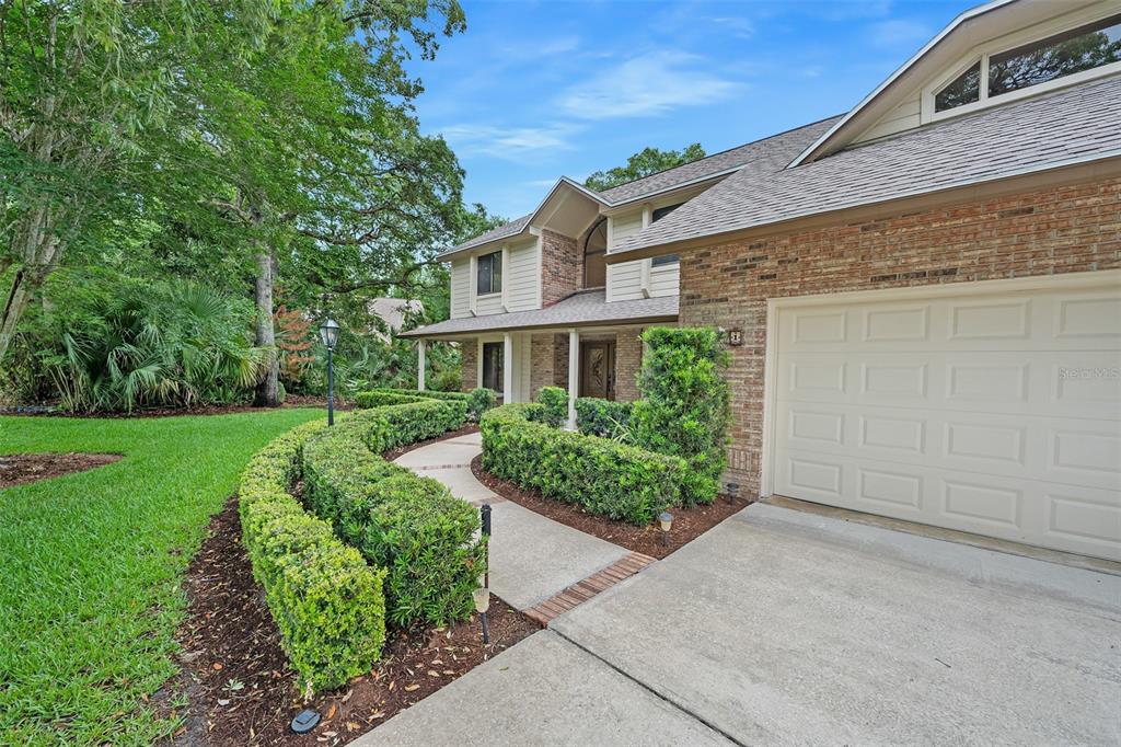 A two-story brick and siding house with a curved hedge-lined walkway and attached garage — 1 CROOKED BRIDGE WAY, ORMOND BEACH, FL