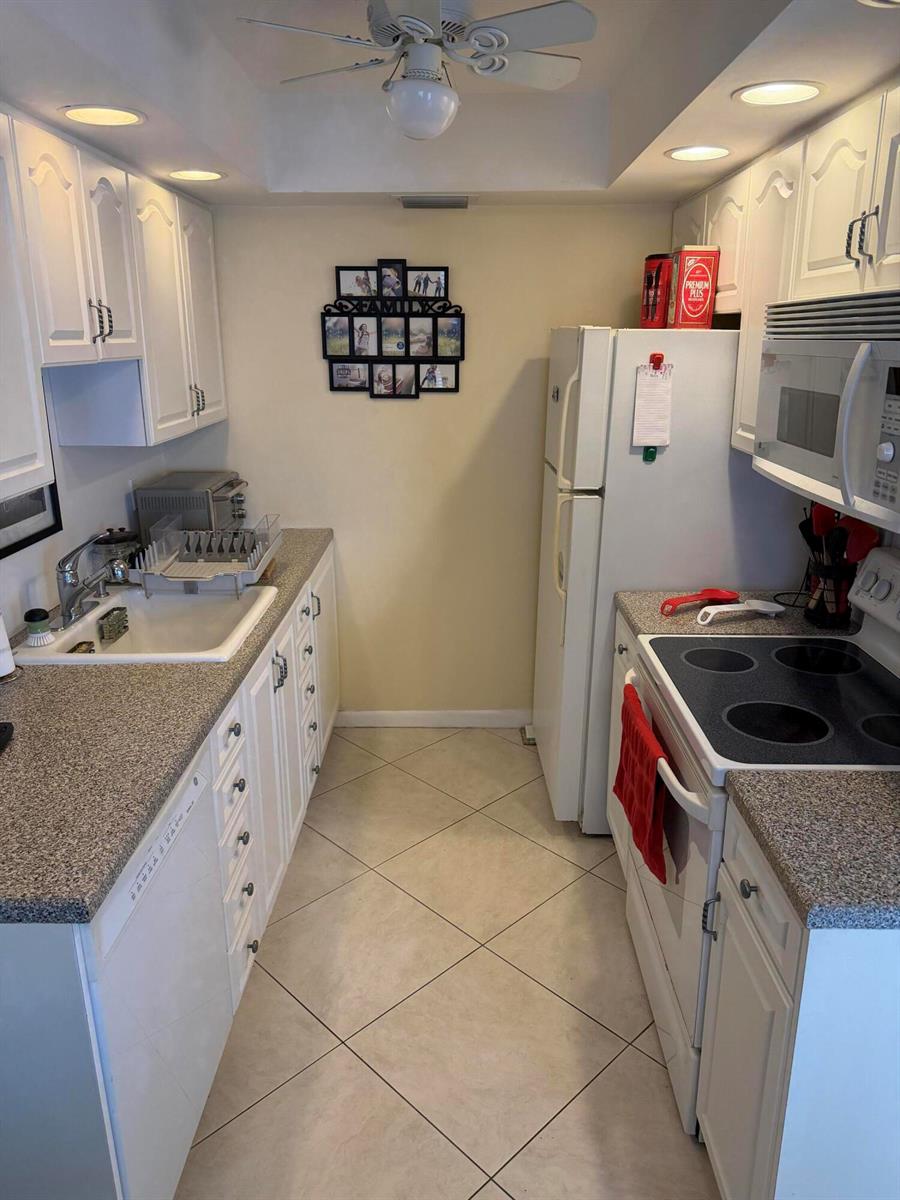 A galley kitchen features white cabinets, speckled countertops, a white refrigerator, and tile flooring — 4042 Exeter C, Boca Raton FL 33434, BOCA RATON, FL