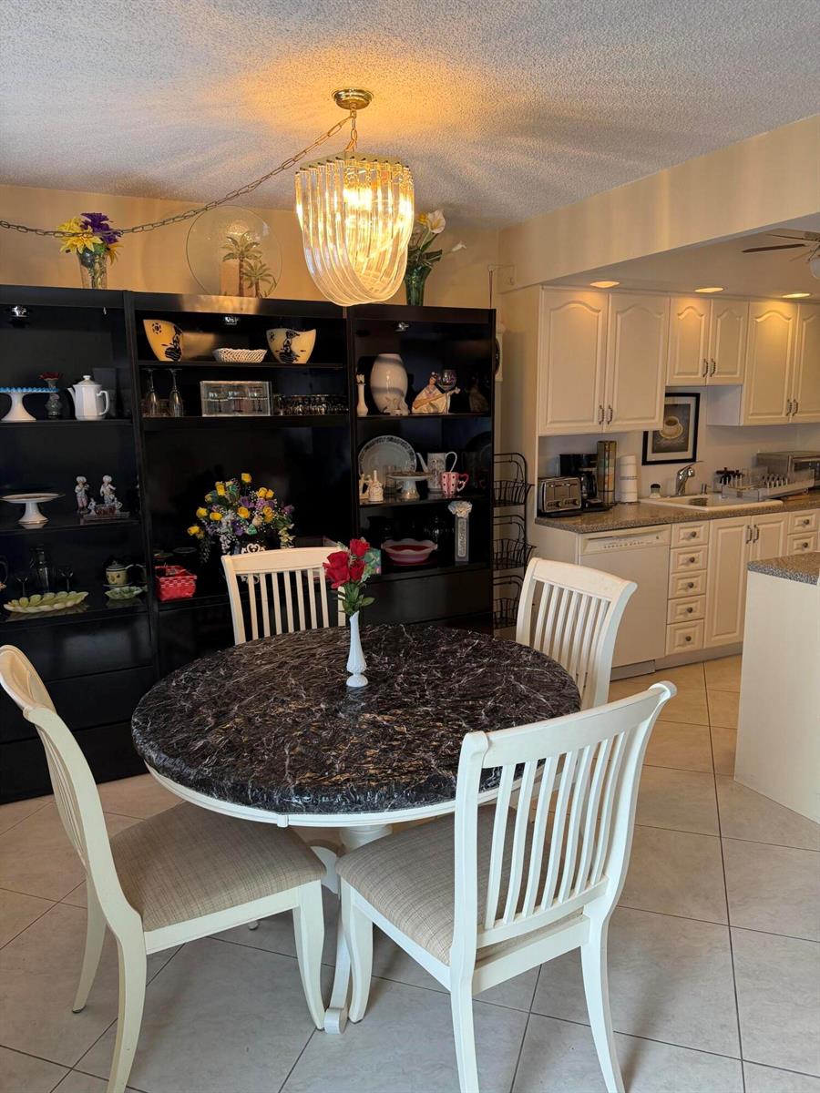 A dining area with a round marble-topped table, white chairs, and a black display cabinet — 4042 Exeter C, Boca Raton FL 33434, BOCA RATON, FL