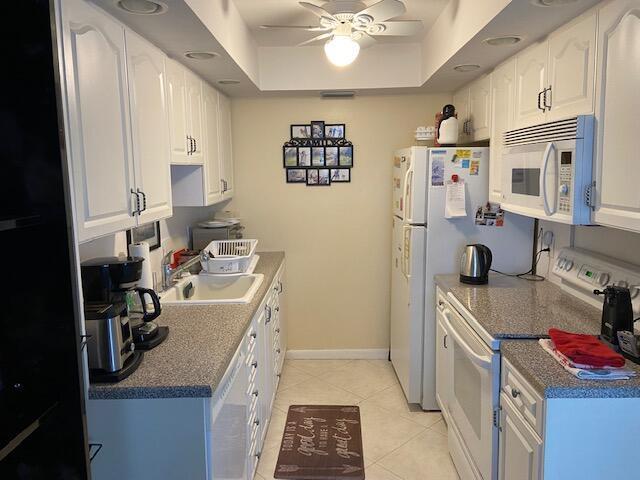 A galley kitchen features white cabinets, granite countertops, a white refrigerator, and a ceiling fan — 4042 Exeter C, Boca Raton FL 33434, BOCA RATON, FL