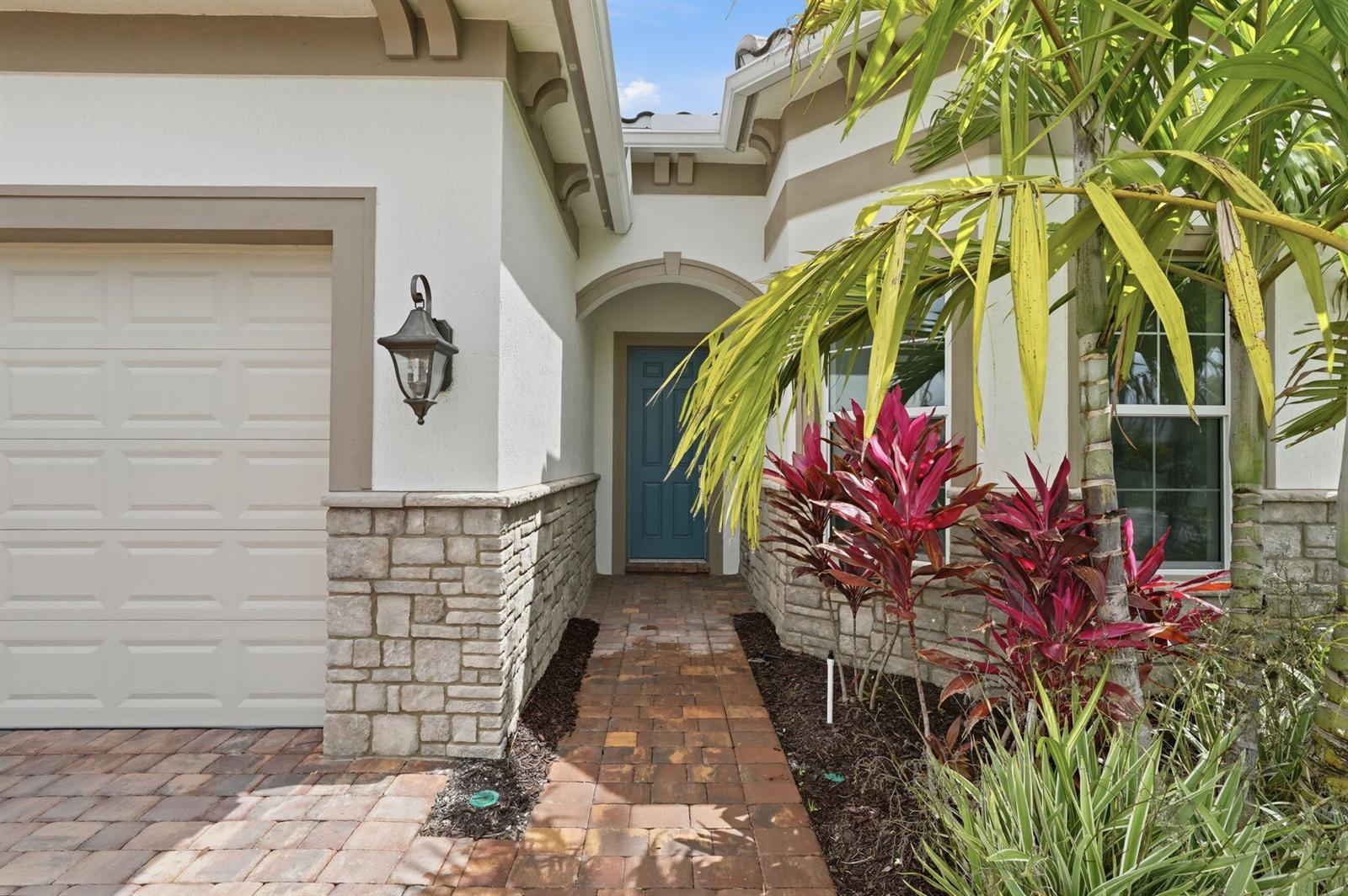 A paved walkway leads to a blue front door beside a garage and stone facade — 10550 Northbrook Circle, Palm Beach Gardens FL 33412, PALM BEACH GARDENS, FL