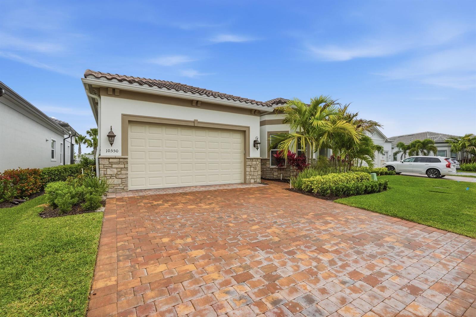 A single-story house with a beige garage, stone accents, and a brick paver driveway — 10550 Northbrook Circle, Palm Beach Gardens FL 33412, PALM BEACH GARDENS, FL