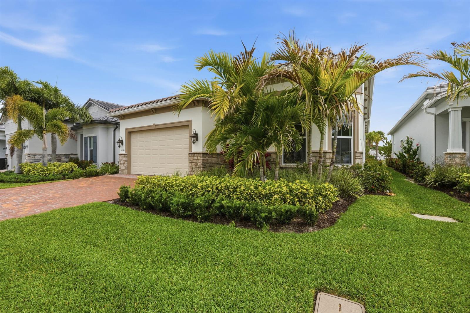 A single-story house with a beige garage, stone accents, and palm trees in the front yard — 10550 Northbrook Circle, Palm Beach Gardens FL 33412, PALM BEACH GARDENS, FL