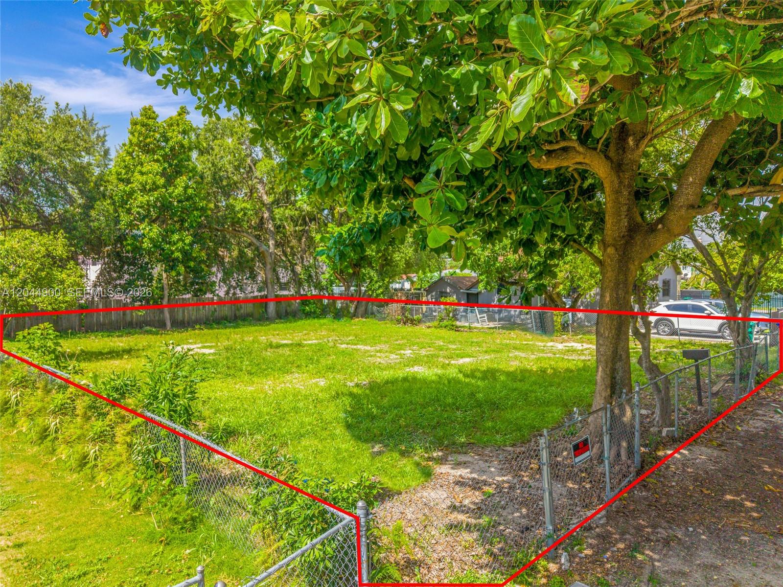 A vacant, grass-covered lot is enclosed by a chain-link fence under large shade trees — 60 NE 76th St, Miami FL 33138, MIAMI, FL