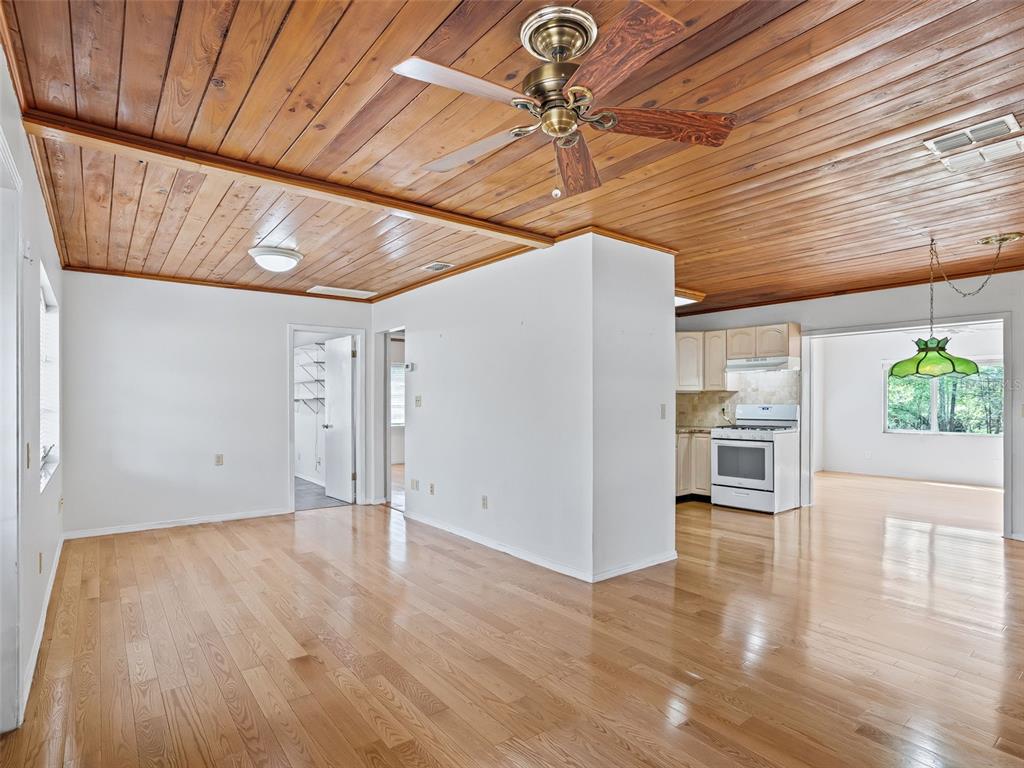 A living room with wood-plank ceilings, hardwood floors, and an adjacent kitchen — 8701 CR 647 S, BUSHNELL, FL
