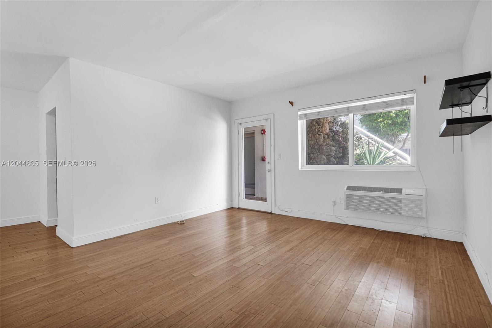 An empty room features light wood flooring, white walls, a window, and a glass door — 320 85th St # 4, Miami Beach FL 33141, MIAMI BEACH, FL