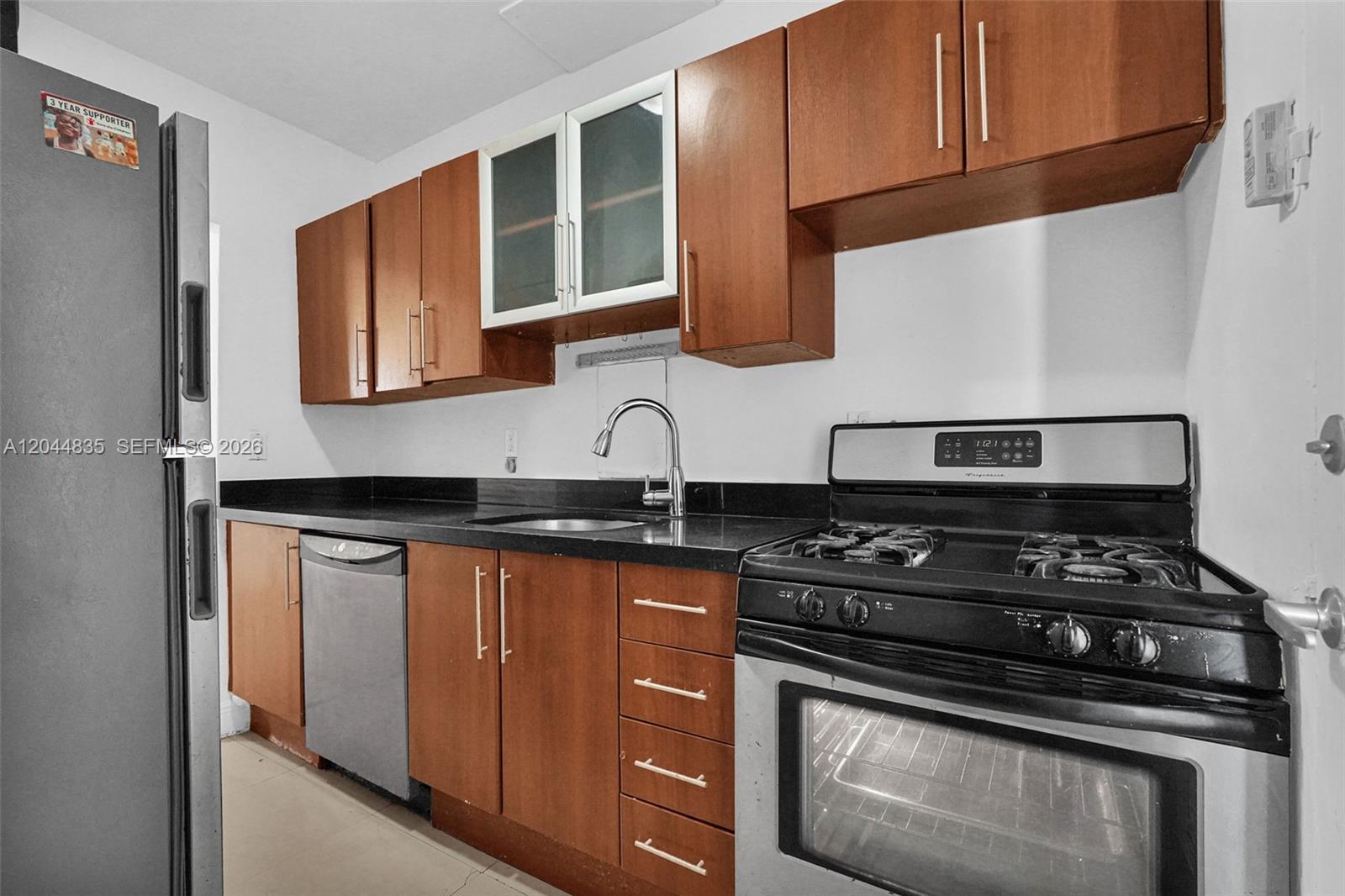 A kitchen features wood cabinets, black countertops, a stainless steel dishwasher, and a gas range — 320 85th St # 4, Miami Beach FL 33141, MIAMI BEACH, FL