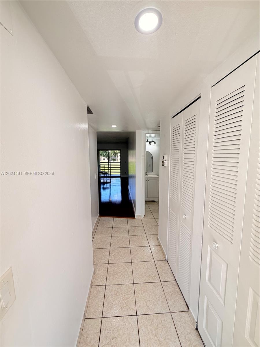 A hallway with tiled floors leads to a bathroom and a dark-floored living area — 2793 NW 104th Ave # 204, Sunrise FL 33322, SUNRISE, FL