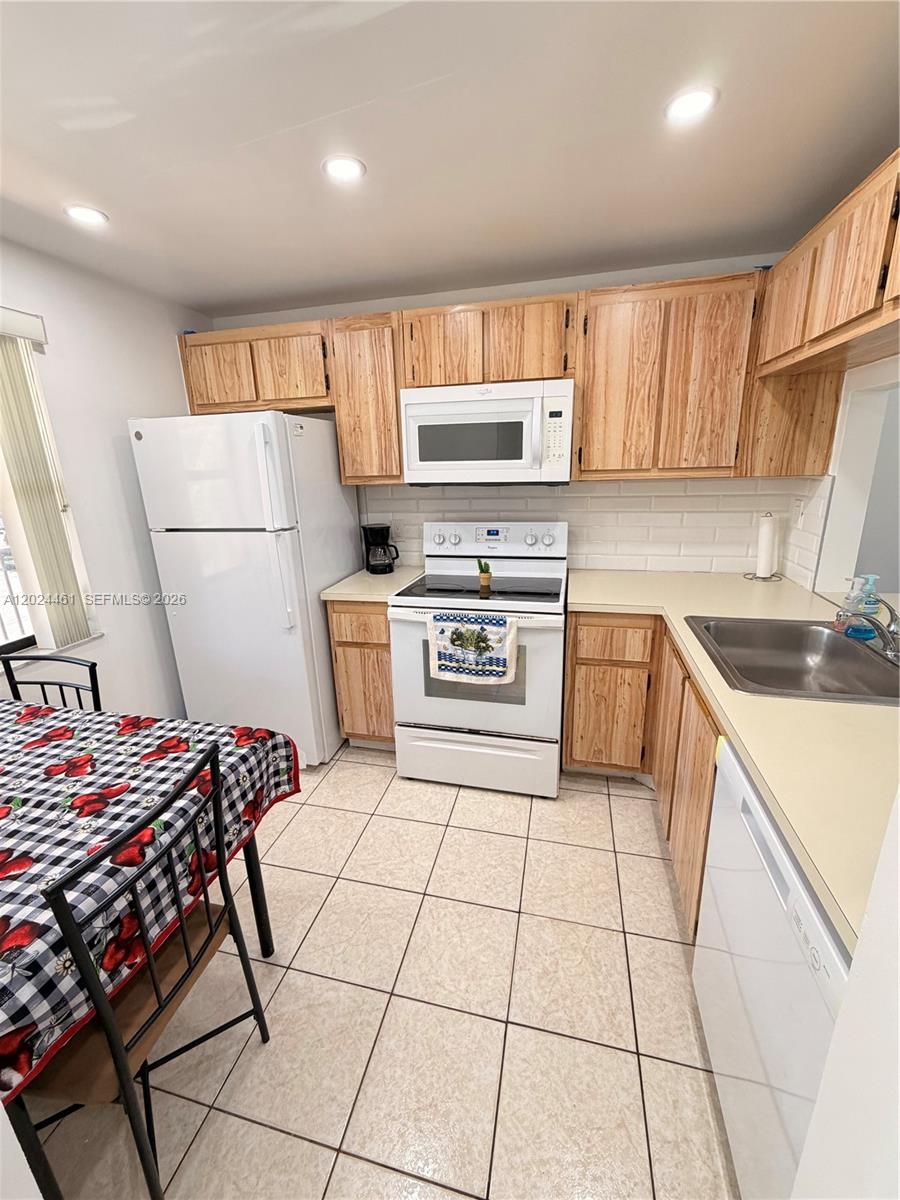 A kitchen features light wood cabinets, white appliances, a tiled backsplash, and a dining table — 2793 NW 104th Ave # 204, Sunrise FL 33322, SUNRISE, FL
