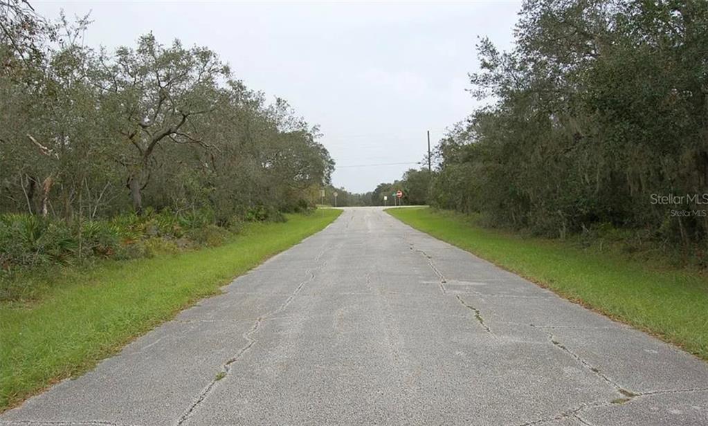 A paved road stretches forward between wooded areas toward a distant intersection — 0 ST JOHNS COURT, POINCIANA, FL