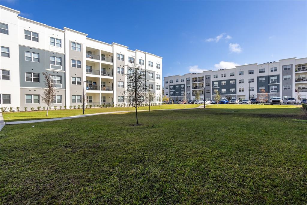 A large grassy courtyard sits between two modern, multi-story apartment buildings under a clear sky — 1230 SOUTHSTATION PLACE UNIT 306, ORLANDO, FL