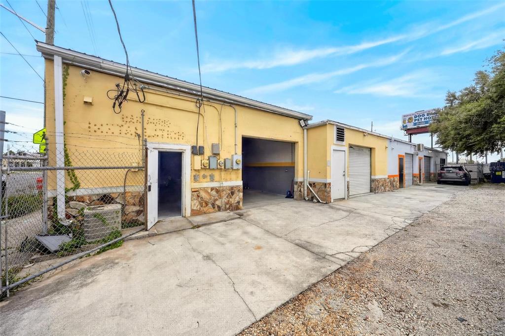 An exterior view of a yellow commercial building with multiple garage bays and a gravel lot — 2906 N ORANGE BLOSSOM TRAIL, ORLANDO, FL