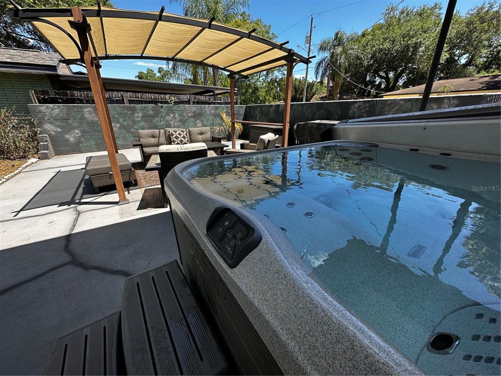 A hot tub sits on a concrete patio next to outdoor furniture under a pergola — 4701 N WILLIS STREET, TAMPA, FL