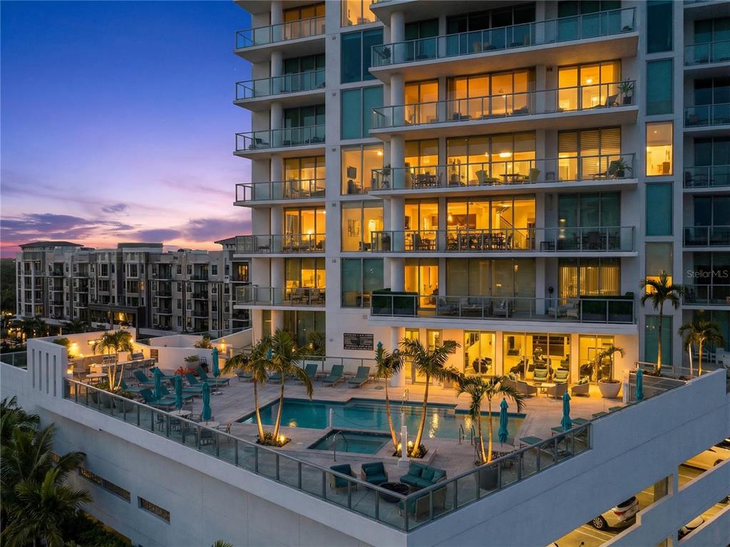 An elevated view of a modern apartment building featuring a rooftop pool and lounge area — 301 QUAY COMMONS UNIT 1807, SARASOTA, FL