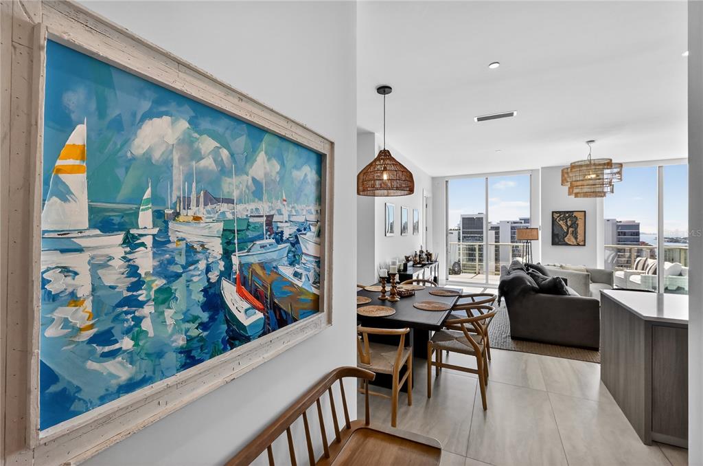 A view from a hallway into an open-concept dining and living area with floor-to-ceiling windows — 301 QUAY COMMONS UNIT 1807, SARASOTA, FL