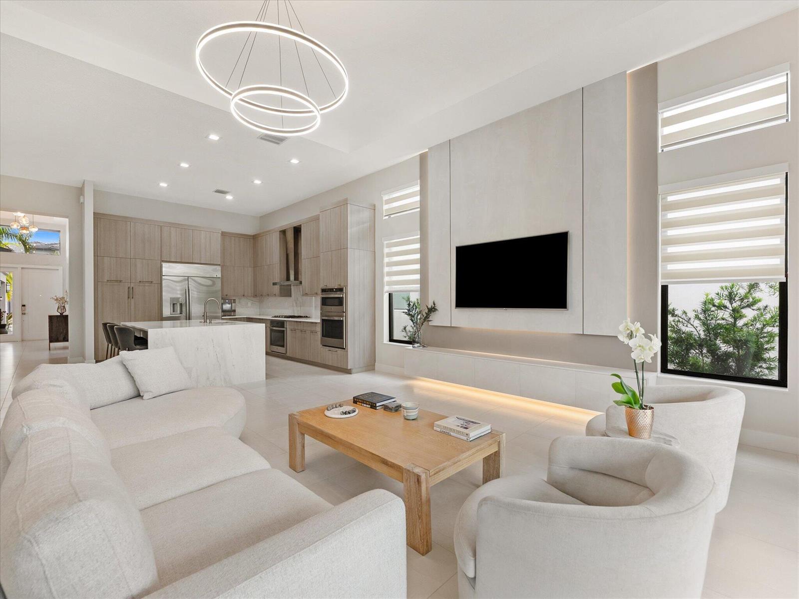 A modern open-concept living room features a light wood coffee table, white sofa, and kitchen — 9273 Sunflower Meadow Road, Boca Raton FL 33434, BOCA RATON, FL