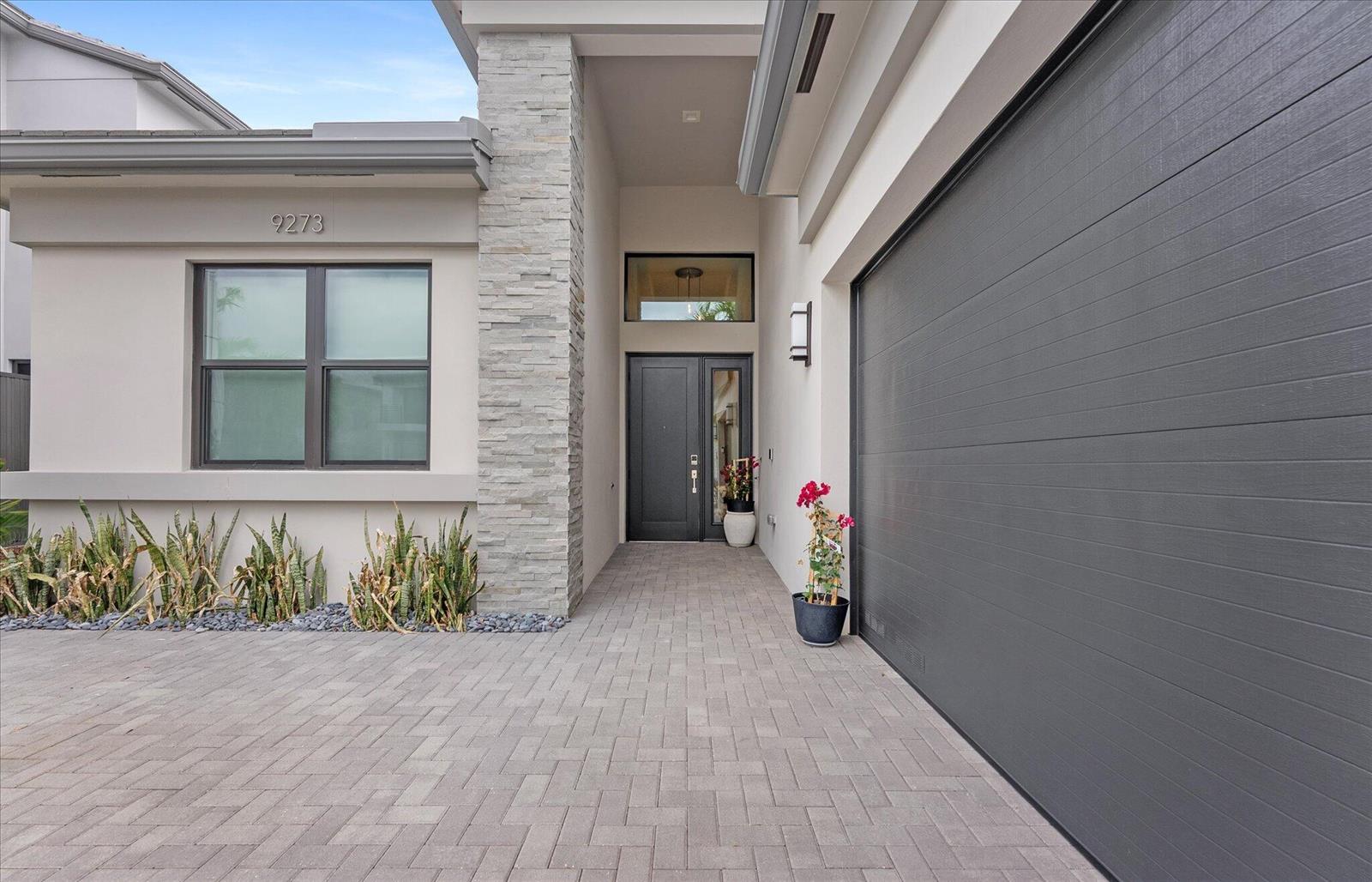 The exterior of a modern home features a stone pillar, gray garage door, and entryway — 9273 Sunflower Meadow Road, Boca Raton FL 33434, BOCA RATON, FL