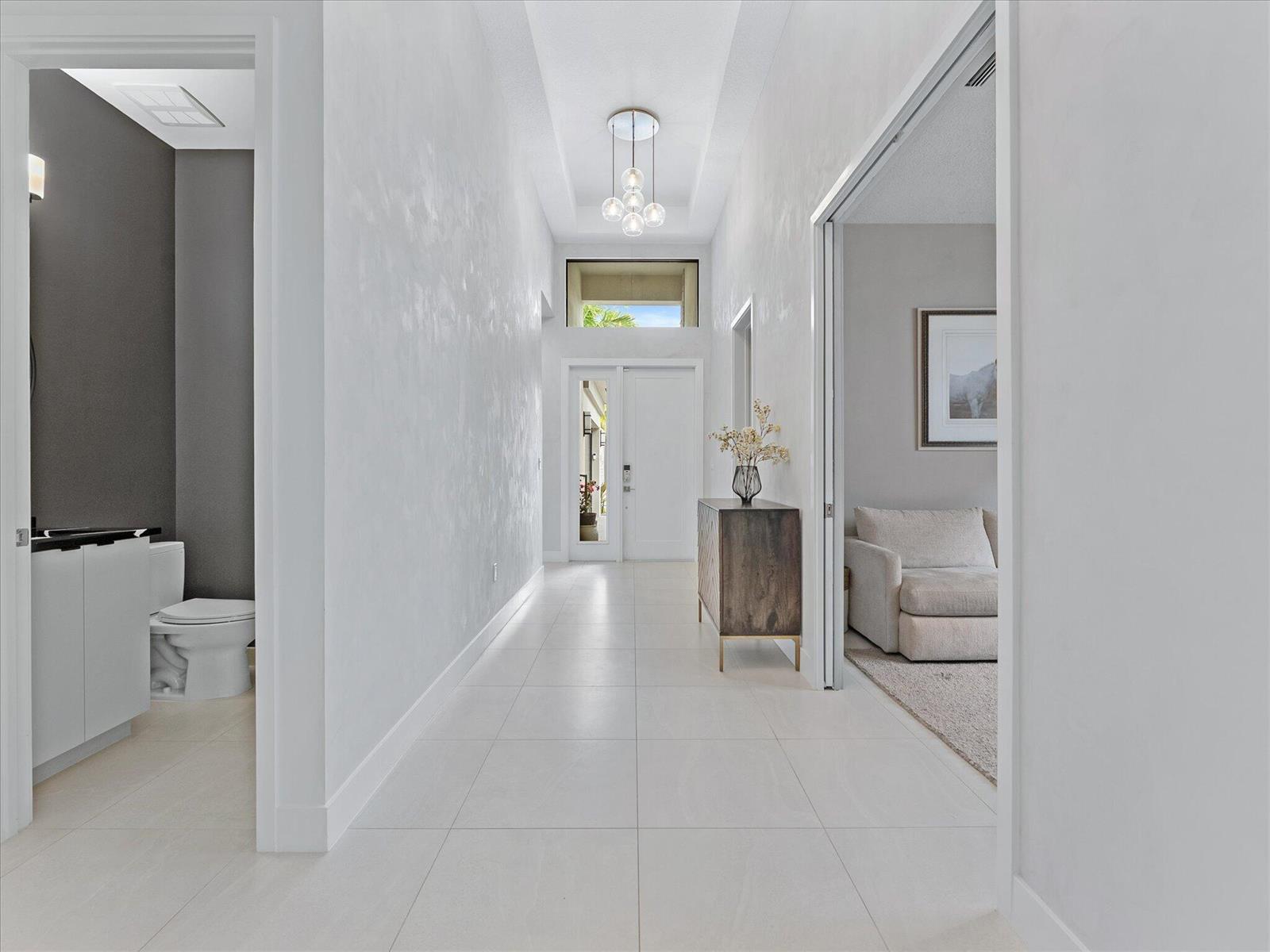 A bright hallway with white tile floors leads to a front door and entryway — 9273 Sunflower Meadow Road, Boca Raton FL 33434, BOCA RATON, FL