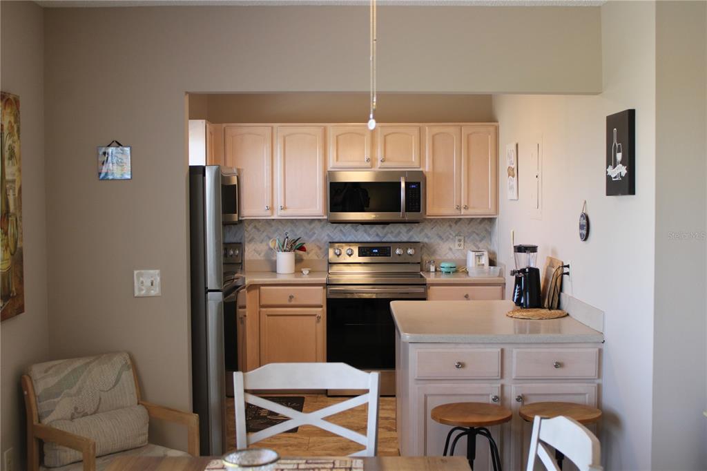 A kitchen features light wood cabinets, stainless steel appliances, and a small breakfast bar — 4460 IRONWOOD CIRCLE UNIT 501A, BRADENTON, FL