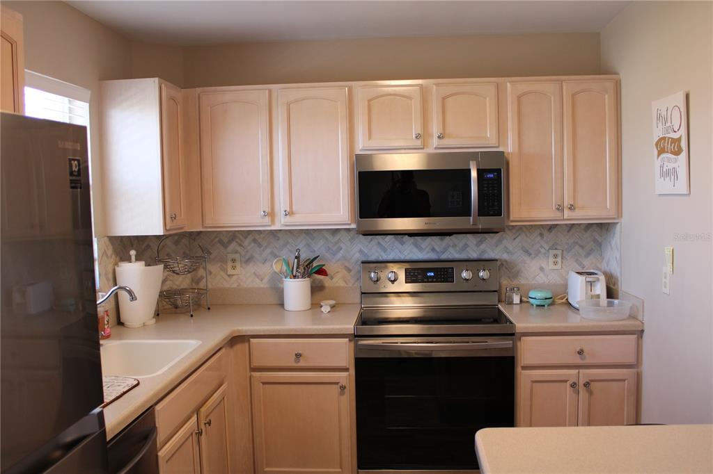 A kitchen features light wood cabinets, stainless steel appliances, and a herringbone-patterned tile backsplash — 4460 IRONWOOD CIRCLE UNIT 501A, BRADENTON, FL