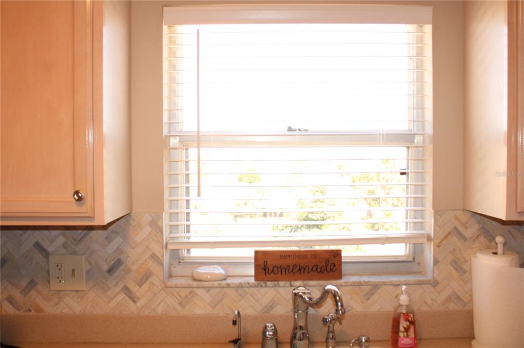 A kitchen sink area features a window with blinds, a backsplash, and wooden cabinets — 4460 IRONWOOD CIRCLE UNIT 501A, BRADENTON, FL
