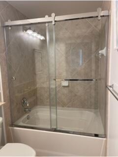 A bathroom featuring a white bathtub with a sliding glass door and beige tile walls — 700 E Boynton Beach Boulevard E # 1509, Boynton Beach FL 33435, BOYNTON BEACH, FL