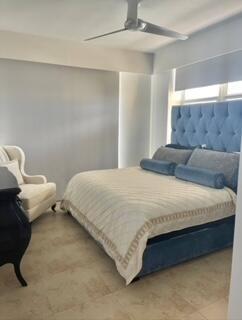 A bedroom features a tufted blue headboard, a cream-colored armchair, and a ceiling fan — 700 E Boynton Beach Boulevard E # 1509, Boynton Beach FL 33435, BOYNTON BEACH, FL