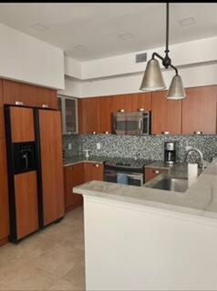 A kitchen features wood cabinets, stainless steel appliances, a mosaic tile backsplash, and a peninsula — 700 E Boynton Beach Boulevard E # 1509, Boynton Beach FL 33435, BOYNTON BEACH, FL